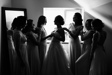 Wedding concept. Black and white photo, bride and bridesmaids posing in hotel or fitting room at wedding day.