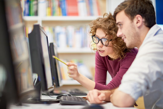 Female college student showing computer program to her classmate during a lesson at computer class at college
