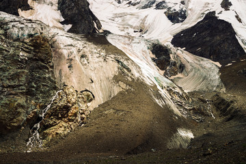 Detailed natural texture of giant rock of fantastic shape covered with snow and ice in highlands. Small waterfalls and brooks flow down mountainside. Fantasy mountain landscape of majestic nature.