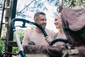parents sitting on bench near baby carriage in park and looking at each other