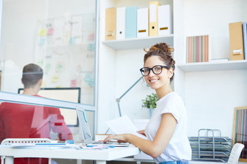 Young successful professional sitting by desk in front of laptop and searching for new online fashion trends