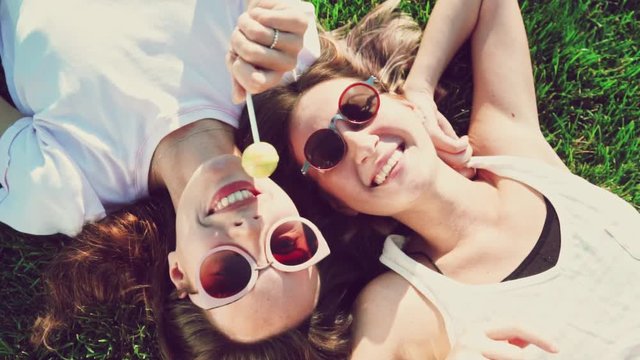 Top view of young woman friends having candy and fun lying on back sharing travel adventure smiling laughing in the park direct from above - summer fashion, leisure and vacation concept