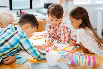 Involved. Joyful classmates drawing pictures while being in a classroom