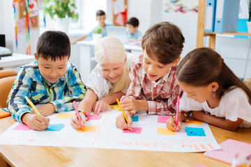 Fototapeta premium Poster. High-spirited joyful children drawing a poster while sitting in a classroom