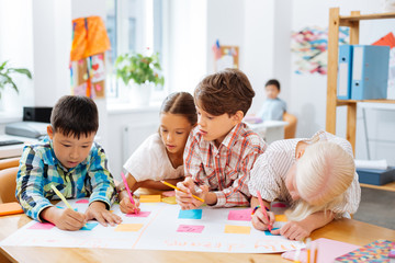 Obraz premium Good mark. Cute sweet kids drawing a new poster in a classroom while preparing a task
