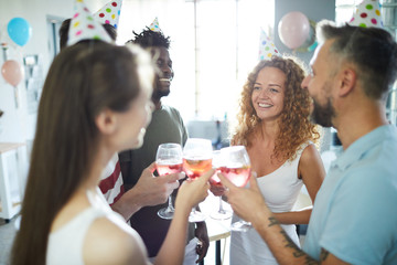 Happy young intercultural friends toasting with homemade drinks at birthday party