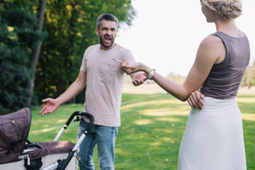 mother smoking cigarette near baby carriage in park, father screaming at her