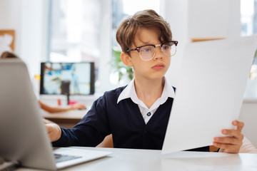 Documents. Clever attentive schoolboy working on a document while sitting in a room