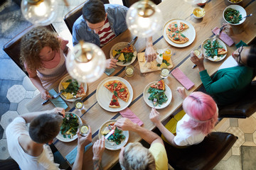 Top view of six casual friends sitting by wooden table served for dinner, enjoying meal and having...