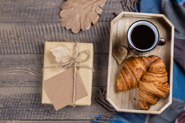 Autumn composition. Black coffee, croissants, gift, plaid on a wooden background. Flat lay, top view, copy space.
