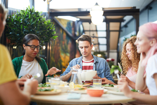 Several young people gathered for dinner by served table in cafe or restaurant