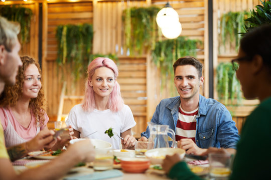 Four companions looking at their friend during conversation by festive dinner in cozy cafe