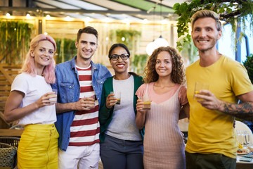 Happy young men and women in casualwear looking at you before toasting
