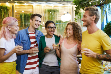 Cute cheerful friends with drinks having talk or discussing toast to make