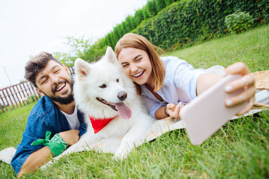 Couple with dog. Young couple lying on the grass making photo with their dog while having traditional picnic