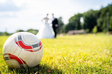 The newlyweds are standing on the soccer field with the ball in the foreground