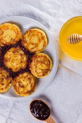 Cottage cheese pancakes on white napkin. Traditional Ukrainian dish - syrniki with jam on a wooden background. Pancakes with cottage cheese on a white plate with honey. Healthy food