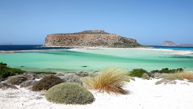 Wind moving the grassland on white sands of Balos beach lagoon on Crete, Greece. Gramvousa island can be seen in the background.