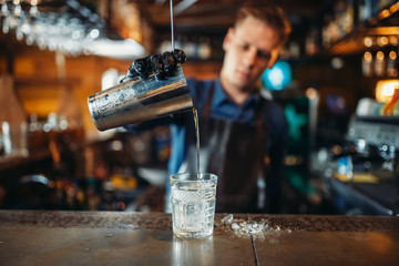 Male bartender in apron pours a drink into a glass