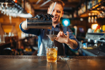 Bartender pours drink through sieve into a glass