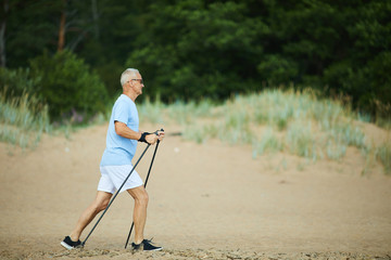 Mature man with grey hair trekking alone along sandy beach on summer day