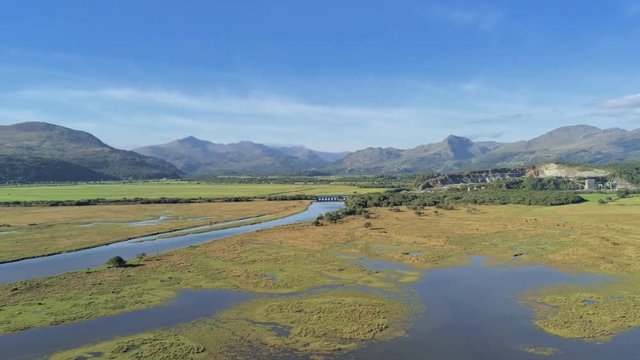 Aerial view, zoom in and out , pan move. Drone panorama over Glaslyn wetlands, quarry, bridge and mountains in background in sunny Wales