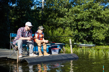 Dad and son fishing at lake in the countryside, they sitting with fishing rods and waiting for catch © pressmaster