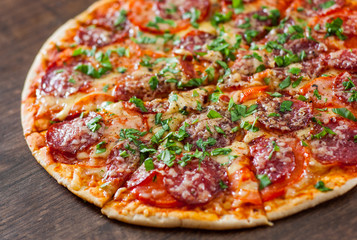sliced Pepperoni Pizza with Mozzarella cheese, salami, Tomatoes, pepper, Spices and Fresh Basil. Italian pizza on wooden background