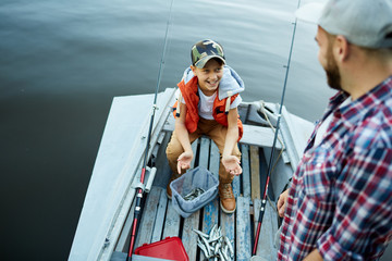 Happy son showing catch to his father while they are in the boat