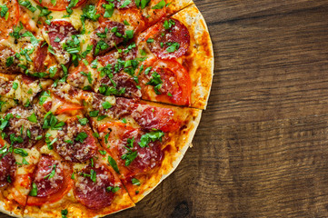 sliced Pepperoni Pizza with Mozzarella cheese, salami, Tomatoes, pepper, Spices and Fresh Basil. Italian pizza on wooden background