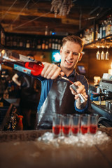 Male barman in apron prepares alcoholic coctail