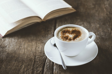 White cup of coffee latte art with cinnamon on wooden table with open book with vintage tone