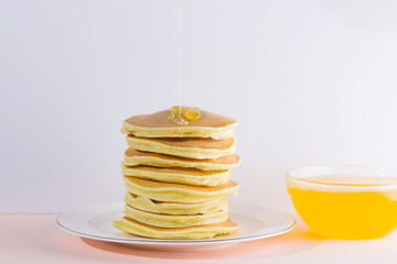 Pancakes on a white pink background. Hot pancakes with honey on a white plate. Delicious dish for breakfast. Honey flows down from a wooden stick on a dish. Healthy food