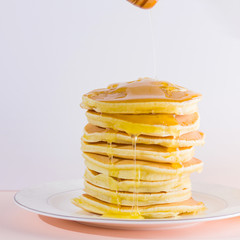 Pancakes on a white pink background. Hot pancakes with honey on a white plate. Delicious dish for breakfast. Honey flows down from a wooden stick on a dish. Healthy food