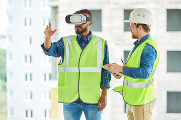Waist up portrait of two modern construction workers using VR gear to visualize projects  on site,...