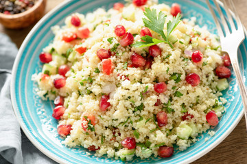 Tabbouleh salad with pomegranate seeds on turquoise plate. Closeup view. Healthy vegetarian arabic salad