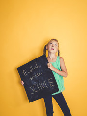 schulkind hält schild oder tafel mit der aufschrift endlich wieder schule vor hintergrund zum schulbeginn