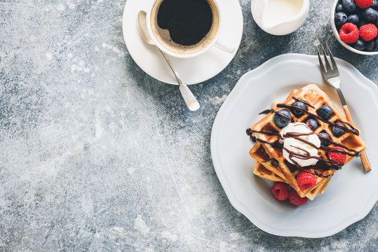 Belgian waffles with ice cream, berries and cup of coffee on concrete background. Top view with copy space for your text. Tasty breakfast