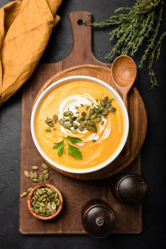 Pumpkin soup in bowl garnished with cream and pumpkin seeds. Top view. Autumn fall comfort food. Cream of pumpkin squash soup