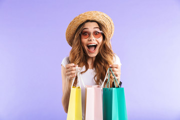 Surprised cute woman isolated over purple wall background holding shopping bags.