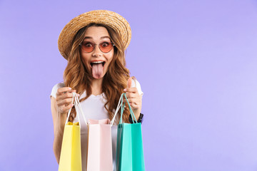Surprised cute woman isolated over purple wall background holding shopping bags.