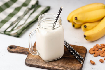 Banana protein smoothie or milkshake in drinking glass on wooden serving board. Closeup view,...