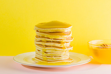 Pancakes with honey on a yellow pink background. Appetizing pancakes on a white plate and honey. Delicious dish for breakfast in the style of pop art. Healthy food