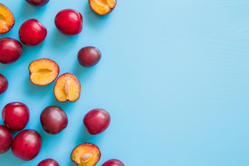 Beautiful, fresh whole and half of plums on the blue background. Healthy sweet food concept. Mock up for fruits offers as advertising or web background, or other ideas. Empty place for text or logo.