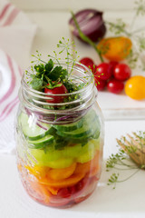 Salad of vegetables with herbs in a glass jar and fresh vegetables on a table.