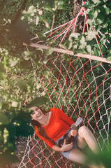 Cheerful woman playing ukulele in hammock at backyard seen through branches