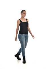 full length portrait of brunette girl wearing black single and jeans. standing pose facing the camera. isolated on white studio background.