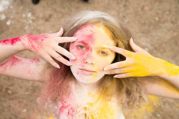 a bright girl with lush hair smiles, her hair, face and hands in the colors of Holi 