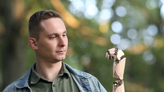 Young Man Looks on His Robotic Hand in the Park. Beautiful realistic 3d animation. 4K