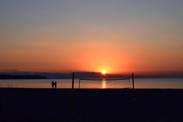Silhouettes next to a volleyball net on the beach. Beautiful sunset in Greece. 